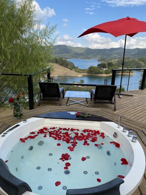 Ein Whirlpool mit Rosenblüten auf einer Holzterrasse mit Blick auf einen See.