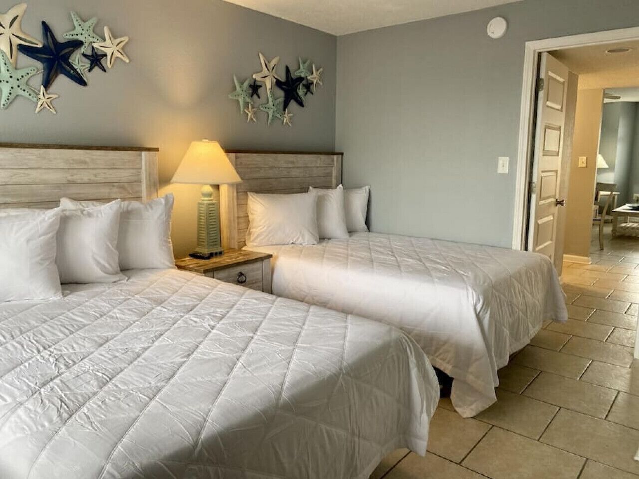 Habitación con dos camas tamaño queen, una mesita de noche con lámpara y decoración de estrellas en la pared.