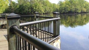 Eine Holzterrasse mit Metallgeländern bietet Blick auf ruhiges Wasser, umgeben von dichtem Baumbestand.