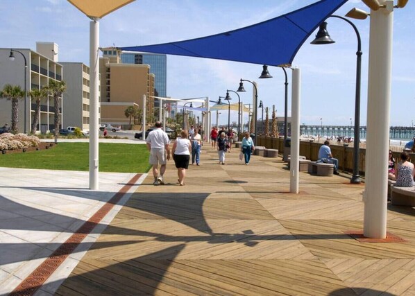 A boardwalk with people walking and sitting, overlooking a body of water.
