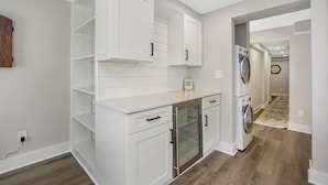 Une cuisine moderne avec des meubles blancs, un four encastré et un lave-linge situé dans la buanderie adjacente.