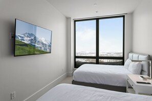Enjoy a panoramic view of the surrounding mountains from the large window, with a flat-screen TV and a comfortable bed with white linens.