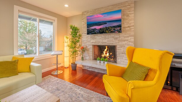 A living room with a fireplace, a sofa, a chair, and a large window. - Spacious remodeled home with central AC and fenced yard (Kirkland)