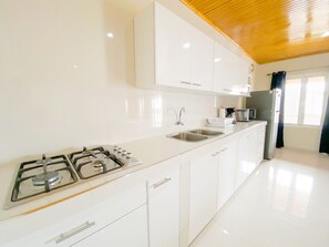 A modern kitchen with white cabinetry, a gas stove, a sink, and a refrigerator.