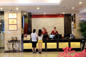 Una recepción de hotel con una recepcionista, una pantalla digital y certificados enmarcados en la pared.