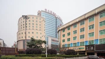 A multi-story hotel with a curved facade, a flat-roofed building adjacent to it, and a parking lot with a white fence.