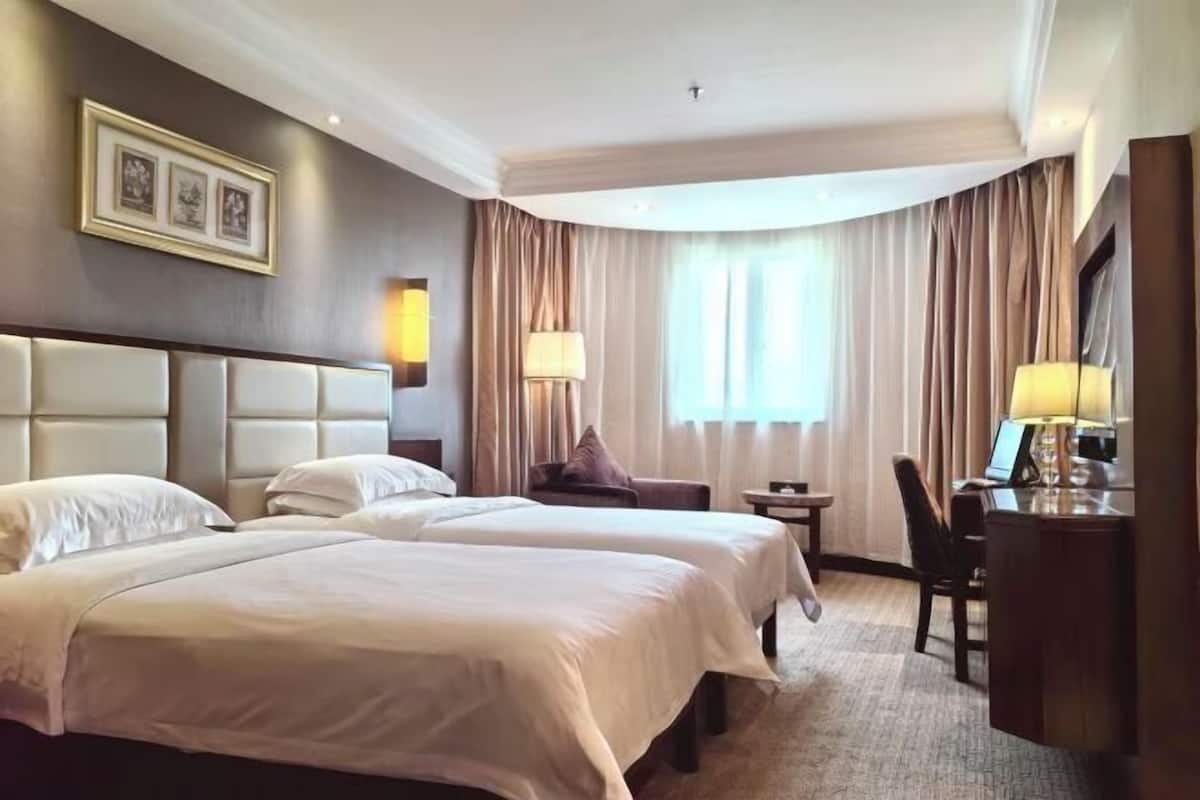 Une chambre d’hôtel avec deux lits, un bureau, une chaise, une lampe et une fenêtre avec des rideaux.