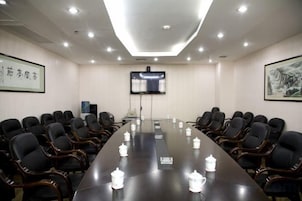 Un salón de conferencias con una larga mesa, sillas, una pantalla de proyector y un cuadro en la pared.