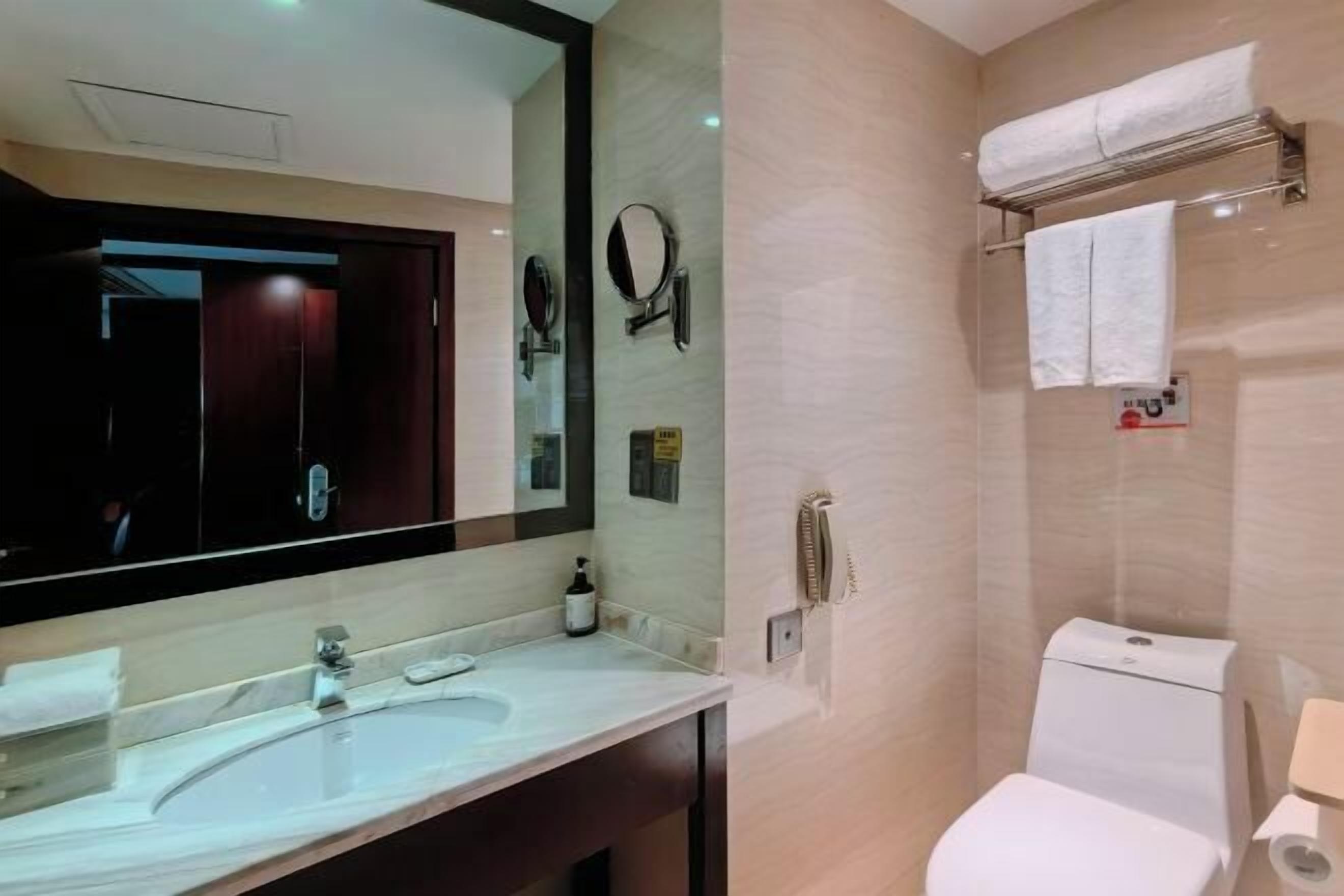 A modern bathroom with a large mirror, a sink, a toilet, and a towel rack.