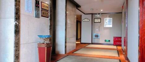 A hotel lobby with a reception desk, a wall-mounted information board, and a carpeted floor.