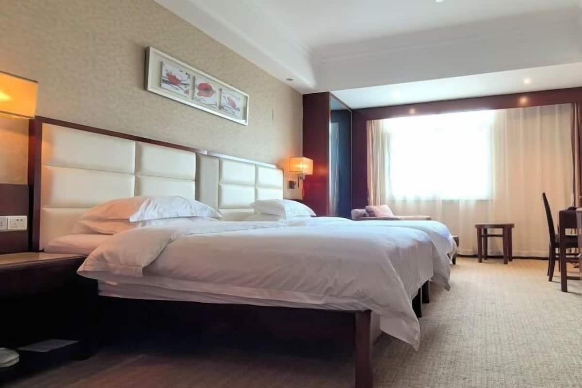 Une chambre d’hôtel avec un grand lit, des tables de chevet, un bureau et une fenêtre avec des rideaux.