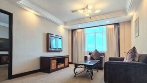 A hotel room with a large window, a flat-screen TV mounted on the wall, a dark-colored sofa, a small table, and a ceiling fan. - Shen Long Mei Du Hotel (Hengyang)