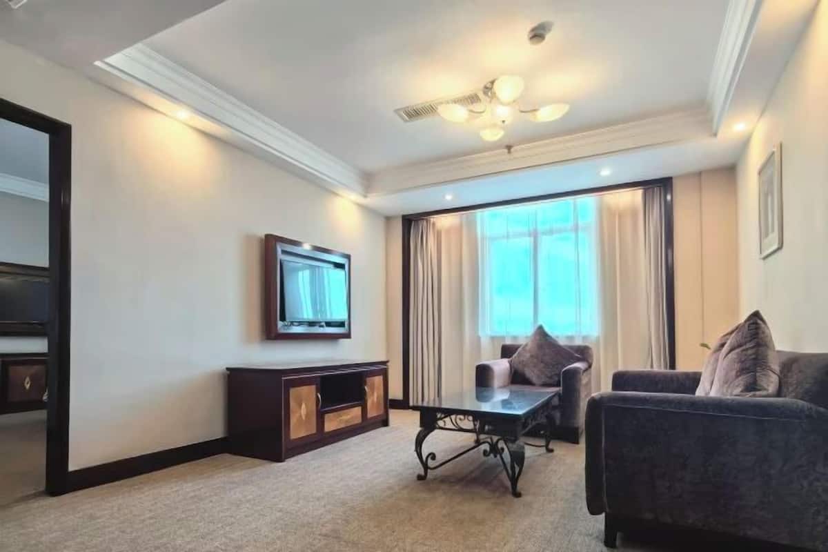 Une chambre d’hôtel dotée d’une grande fenêtre, d’un téléviseur à écran plat fixé au mur, d’un canapé de couleur sombre, d’une petite table et d’un ventilateur de plafond.