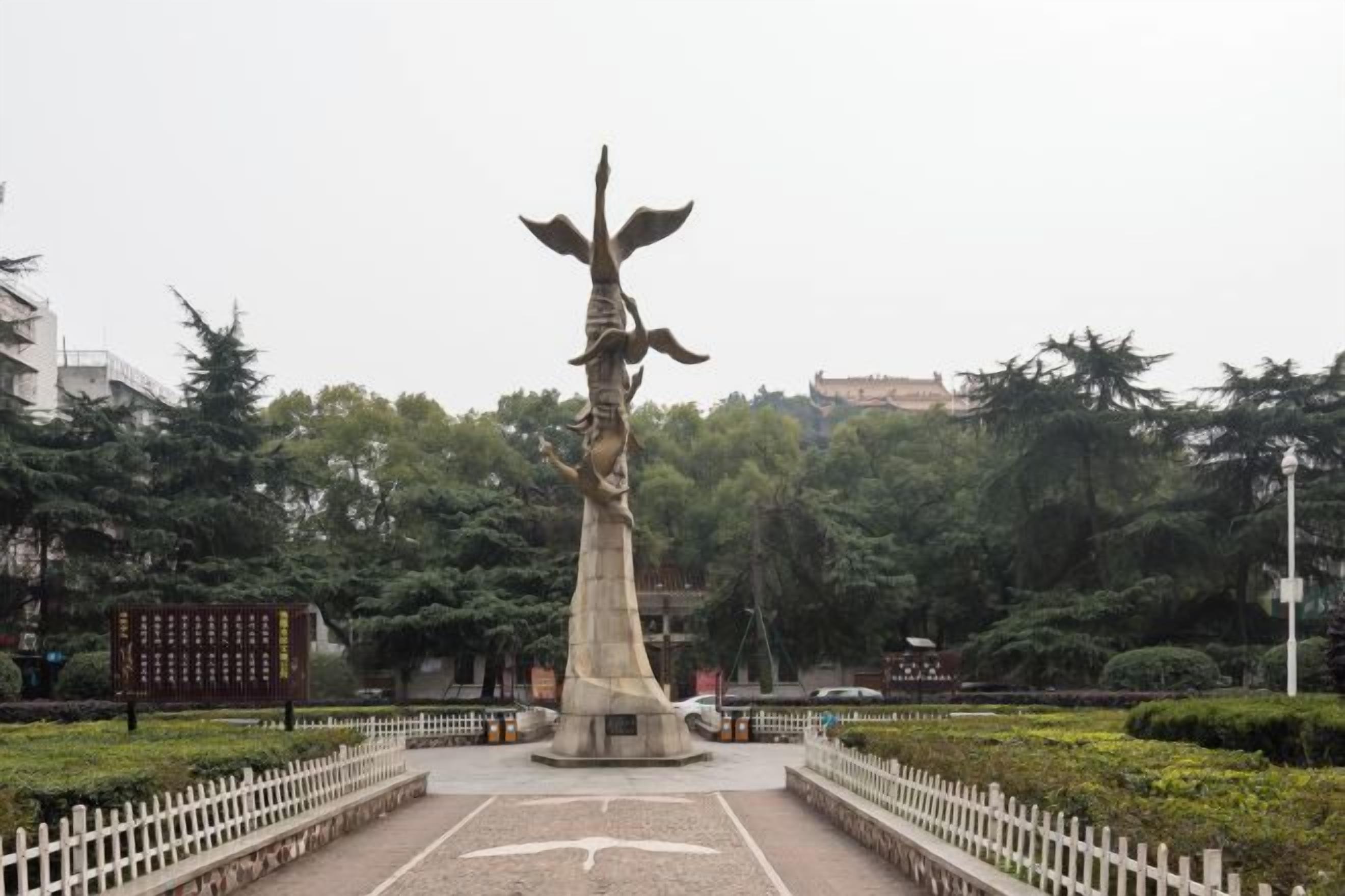 Un parco con un monumento centrale, circondato da un recinto bianco e da vegetazione.