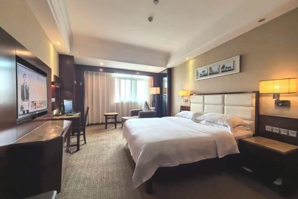 Une chambre d’hôtel équipée d’un lit, de tables de chevet, d’un bureau, d’une chaise, d’une télévision et d’une fenêtre avec des rideaux.