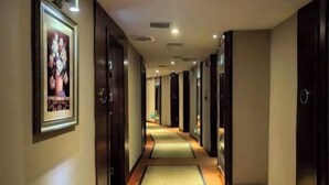 A hotel hallway with framed artwork on the walls, a carpeted floor, and doors leading to rooms. - Shen Long Mei Du Hotel (Hengyang)