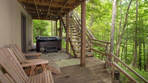 Eine Holzterrasse mit Whirlpool, Holzstühlen und einer Treppe, die in einen Wald führt.