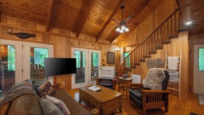 Ein gemütliches Blockhaus-Interieur mit Holzboden, einem Flachbildfernseher, einer Ledersofa, einem Holztisch und einer Treppe.