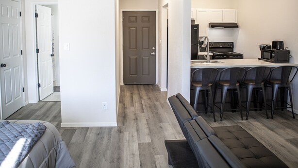 A modern apartment with a living area, a kitchen with bar stools, and a door leading to another room.