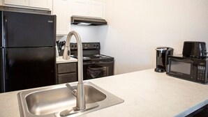 A kitchen with a stainless steel sink, a black refrigerator, a stove, and a microwave.