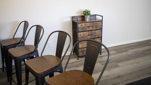 A dining area with four metal chairs and a wooden table, a small metal cabinet with drawers, and a wall-mounted television.