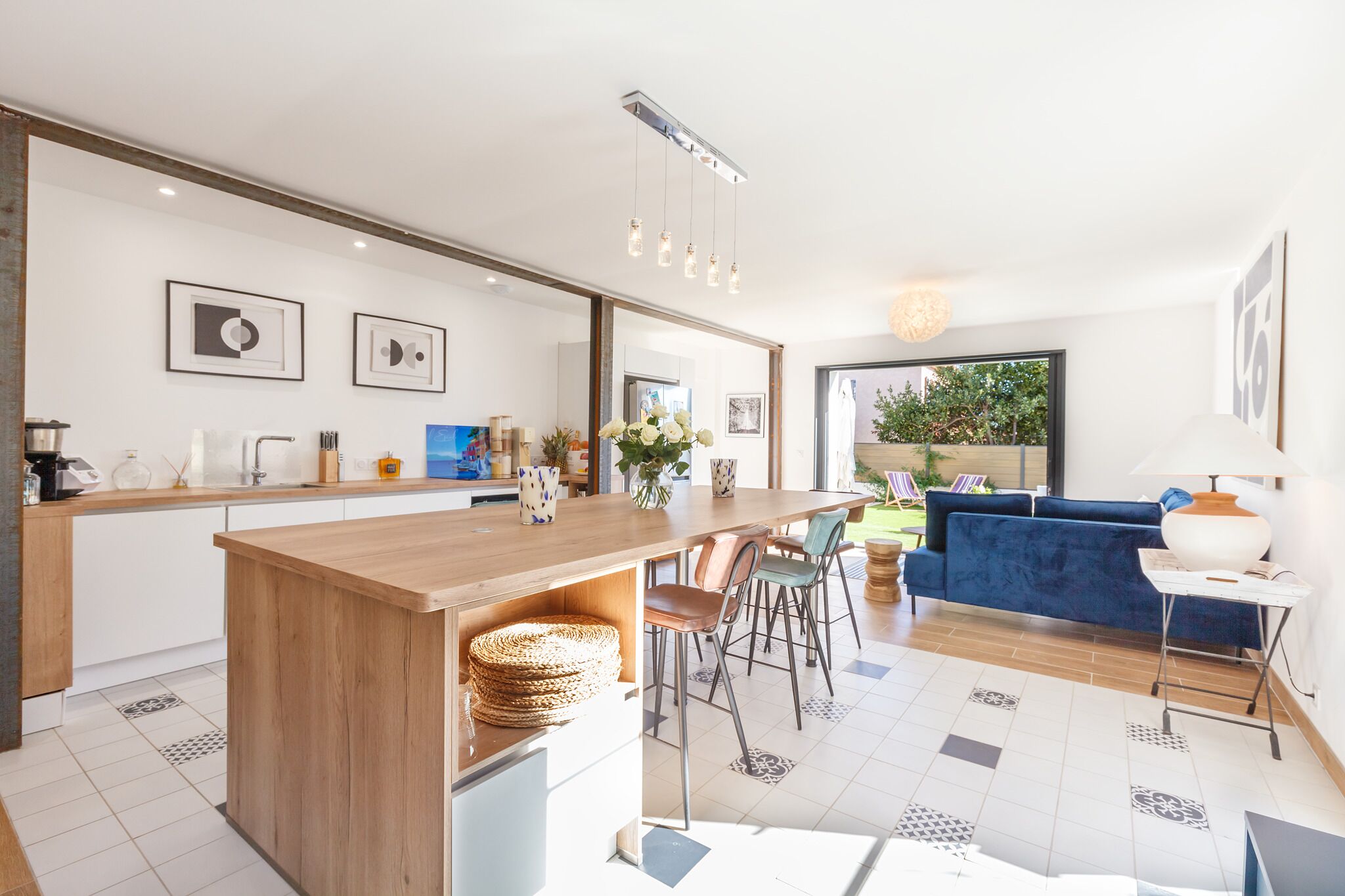 A modern kitchen with a wooden island, a dining area with chairs, and a blue sofa in a living room.
