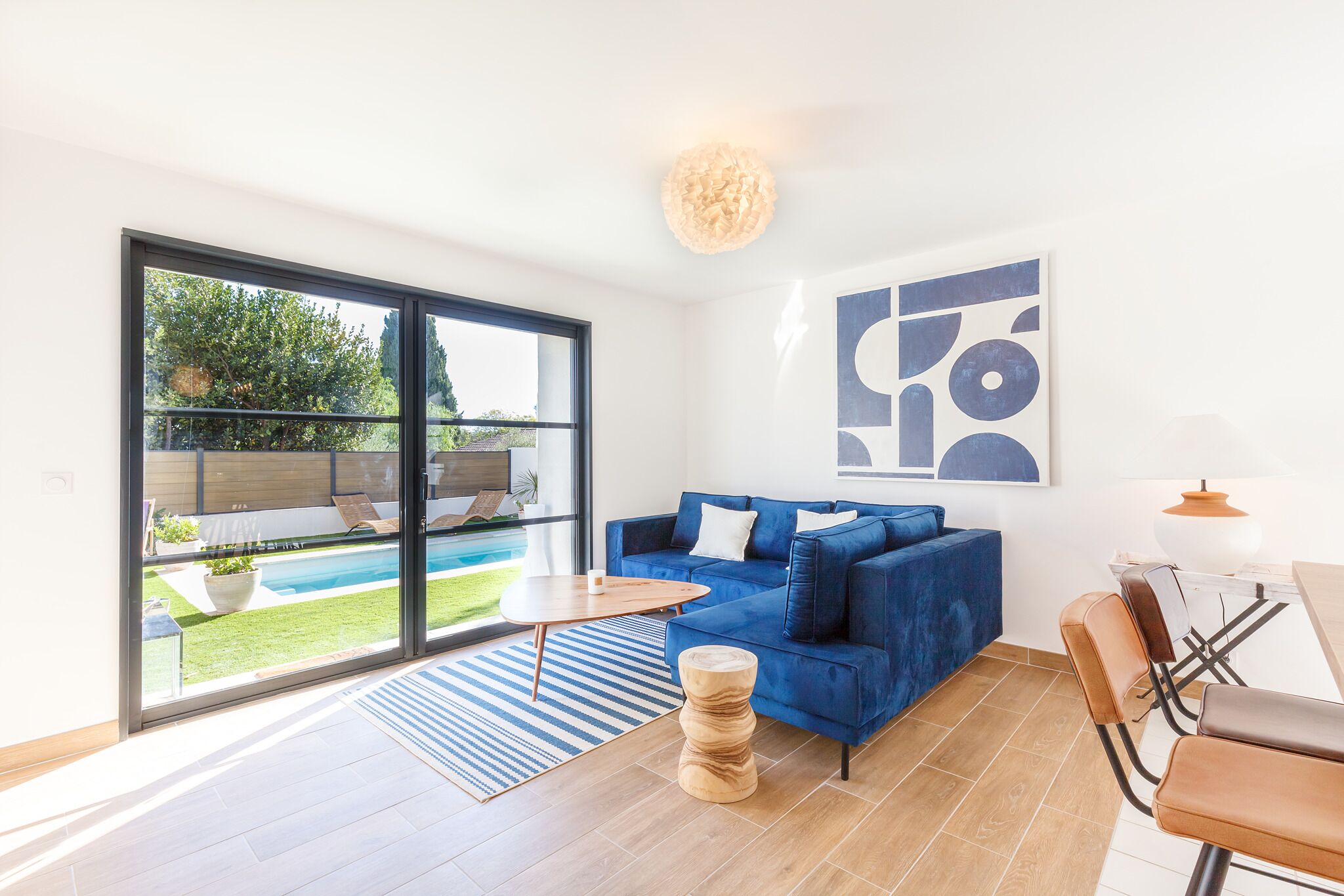 Un salon moderne avec un canapé bleu, une table à manger et une grande fenêtre donnant sur une piscine.