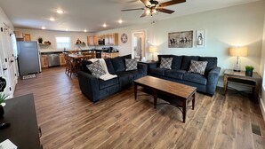 Un salon spacieux avec un grand canapé d’angle gris foncé, une table basse en bois et un ventilateur de plafond.