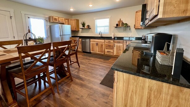 Une cuisine moderne avec des meubles en bois, un plan de travail noir et un coin repas doté de chaises en bois.