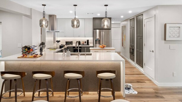 Una cucina moderna con isola centrale, sgabelli da bar, elettrodomestici in acciaio inossidabile, lampade a sospensione e un design pulito e minimalista.
