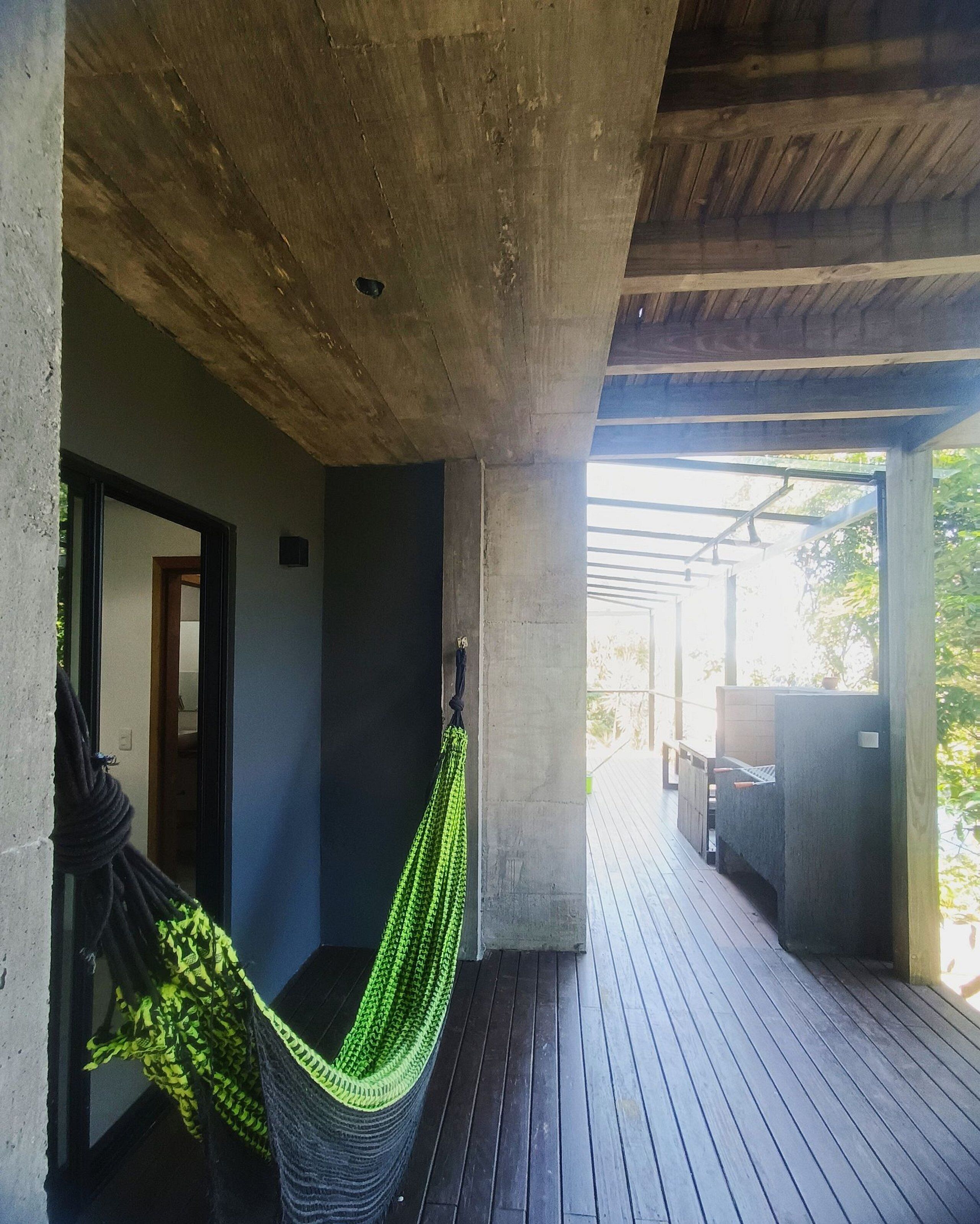 A covered outdoor area with a hammock, wooden deck, and a concrete ceiling.