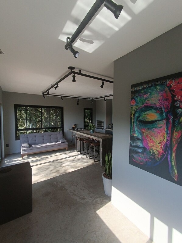 Un espacio habitable moderno con un sofá, zona de comedor y un cuadro abstracto grande.