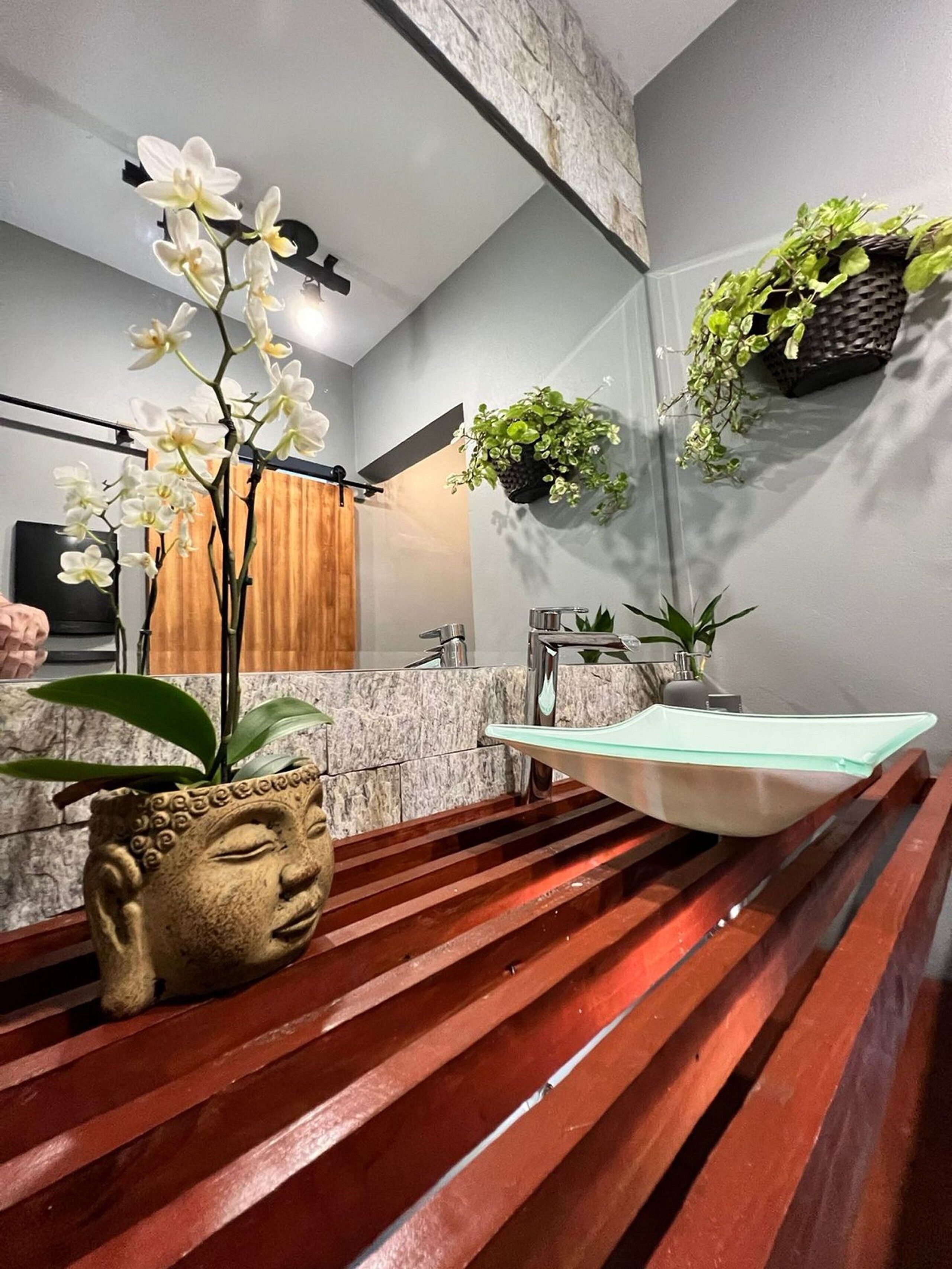 Un baño moderno con encimera de mármol, un banco de madera y diversas plantas.