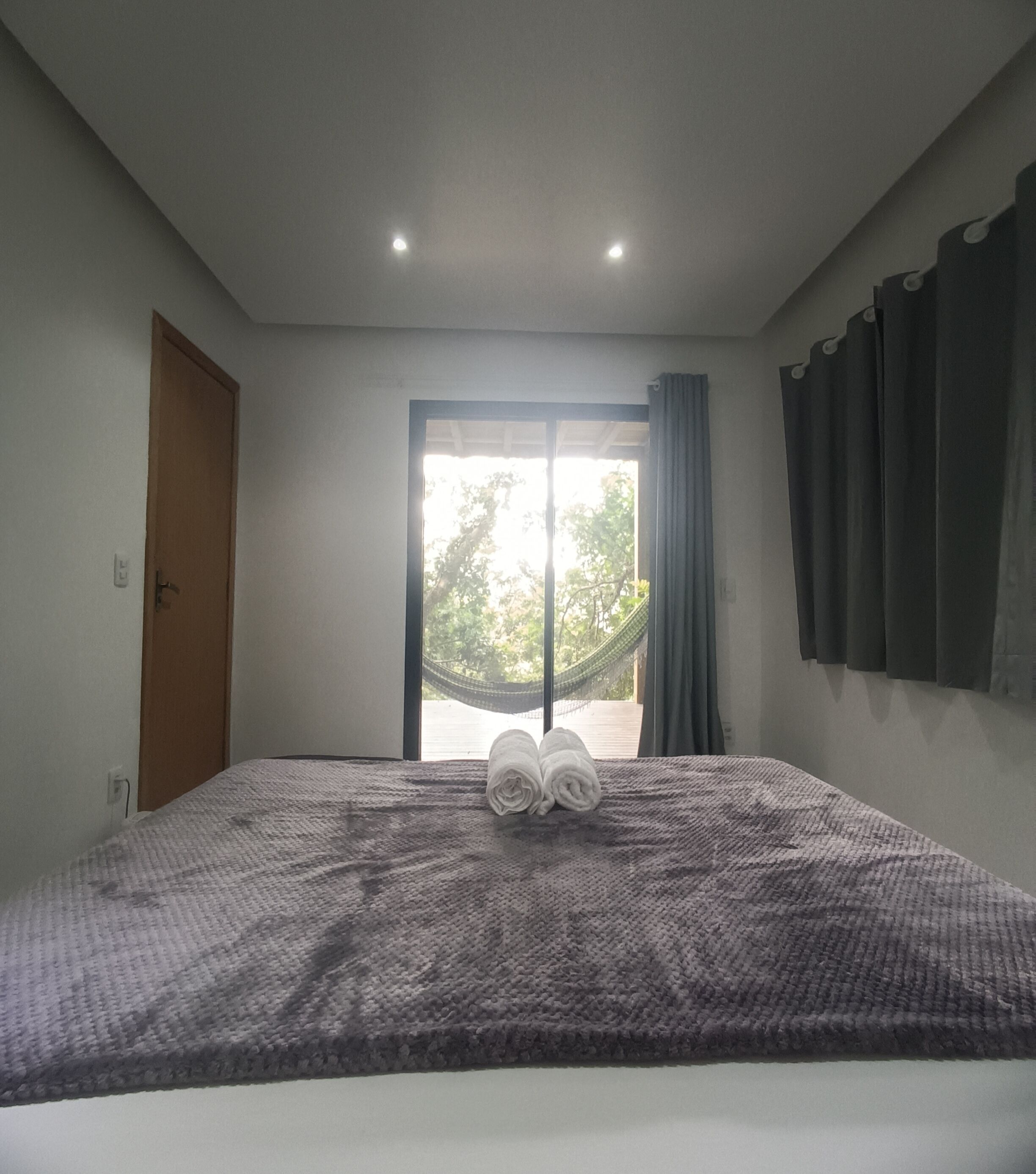 A bedroom with a large bed, a hammock outside the window, and a door on the left.