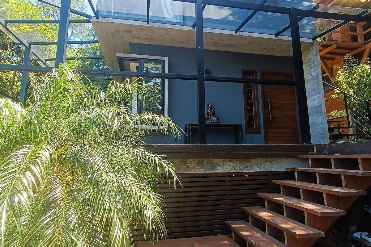Ein modernes, zweistöckiges Haus mit einem Balkon, Holzstufen und einer Statue.