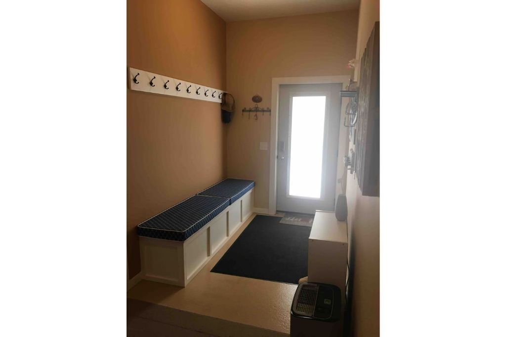 A hallway with a bench, a coat rack, and a door leading to another room.