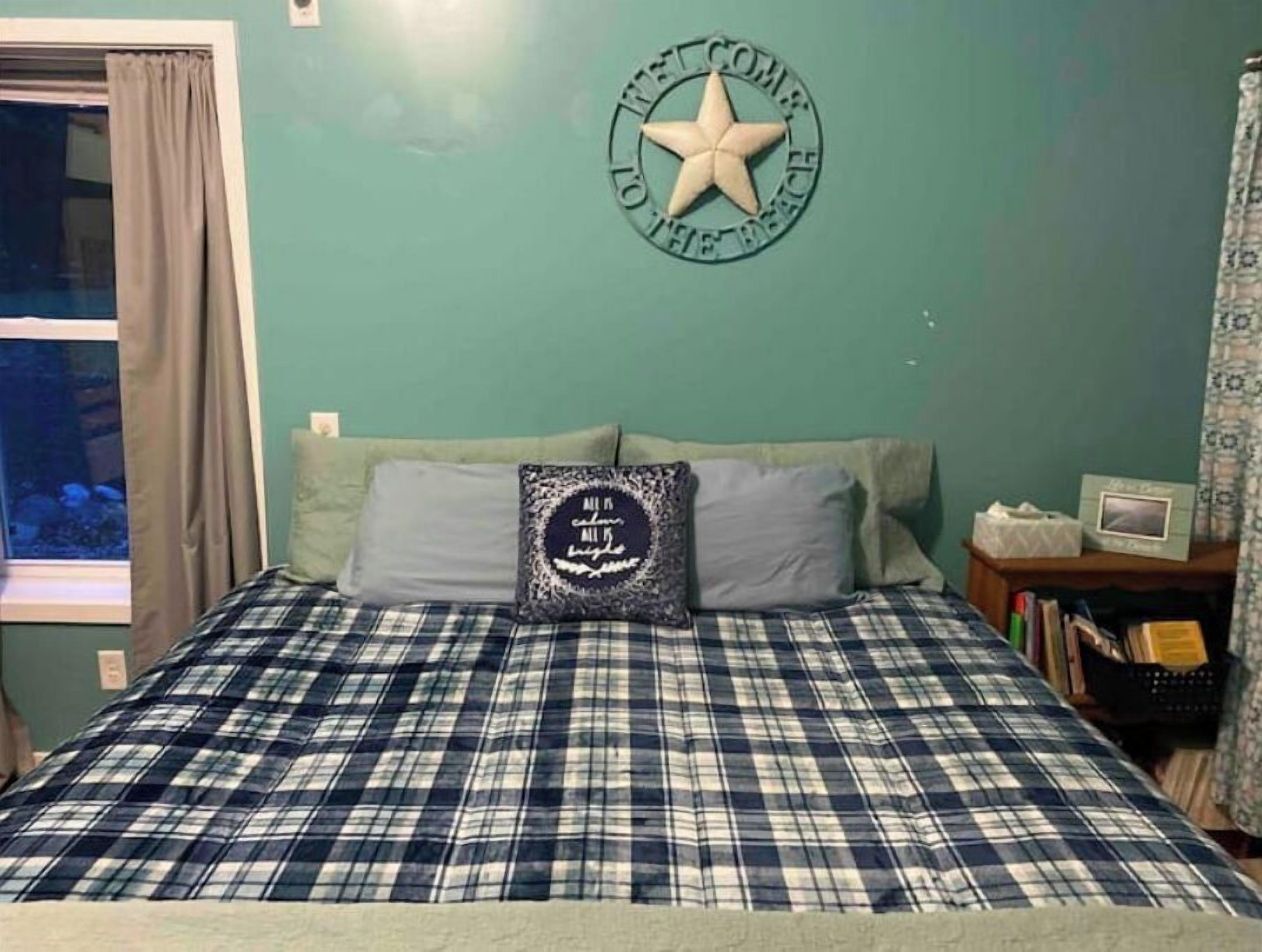 A room with a bed, a pillow with a star design, a wall clock, and a window with curtains.