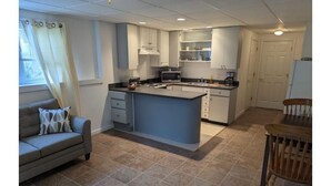 Une cuisine compacte dotée d’un îlot central, de meubles blancs et d’un coin repas avec une table et des chaises en bois.