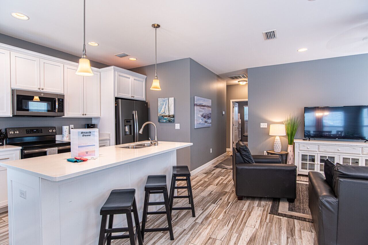 A modern kitchen with white cabinets, a central island with bar stools, a refrigerator, and a microwave.