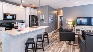 A modern kitchen with white cabinets, a central island with bar stools, a refrigerator, and a microwave.