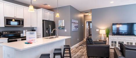 A modern kitchen with white cabinets, a central island with bar stools, a refrigerator, and a microwave.