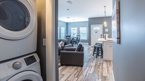 A laundry area with stacked washing machines, a dining area with a table and chairs, and a kitchen with a counter and stools.
