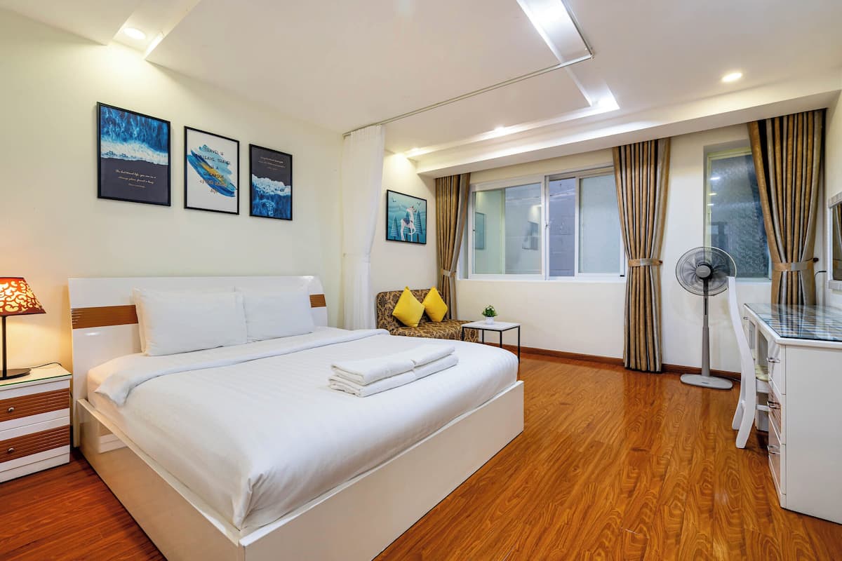 Une chambre d’hôtel avec un grand lit, des tables de chevet, un bureau et une fenêtre avec des rideaux.