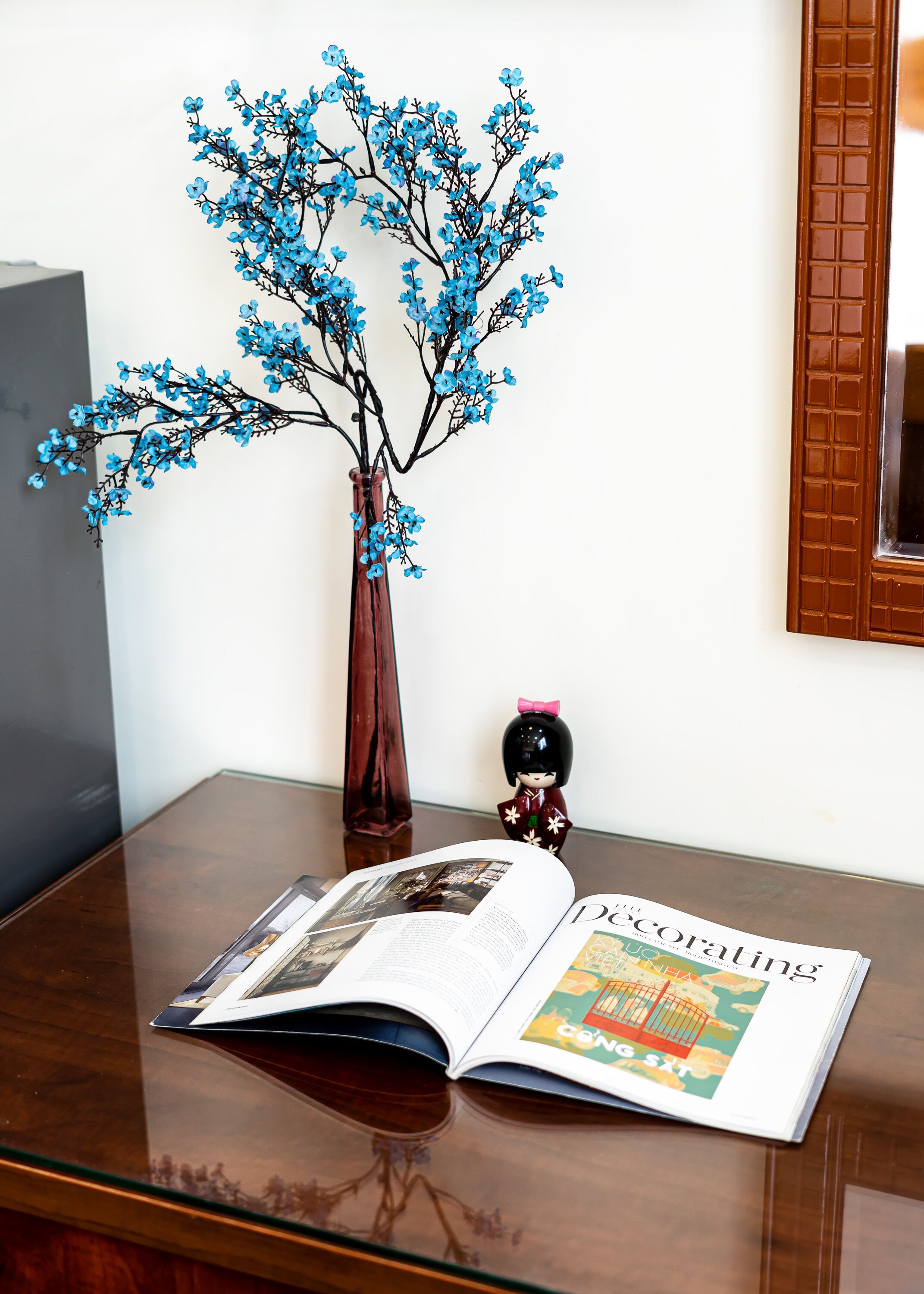 Une table en bois ornée d’un vase décoratif, d’une poupée et d’un magazine ouvert.