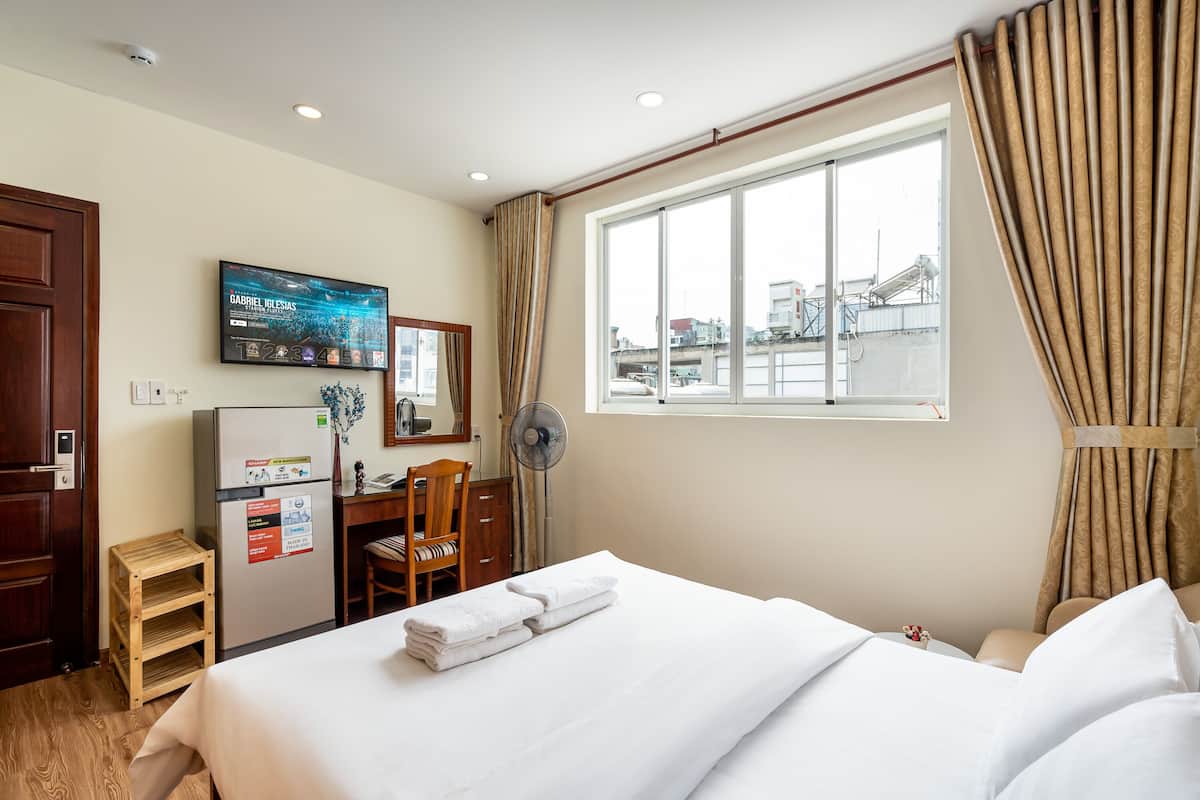 Une chambre d’hôtel équipée d’un lit, d’un bureau, d’une chaise, d’une télévision, d’un ventilateur et d’une fenêtre avec des rideaux.
