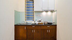 A kitchen with wooden cabinets, a stainless steel sink, and a window with a yellow grill. - WE HOME Japan Town (Ho Chi Minh City)