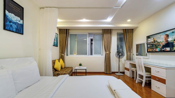 A hotel room with a large bed, a desk, a chair, a TV, and a window with curtains. - WE HOME Japan Town (Ho Chi Minh City)