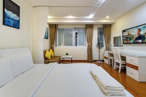 Hotellihuone, jossa on suuri sänky, työpöytä, tuoli, televisio ja ikkuna, jossa on verhot.