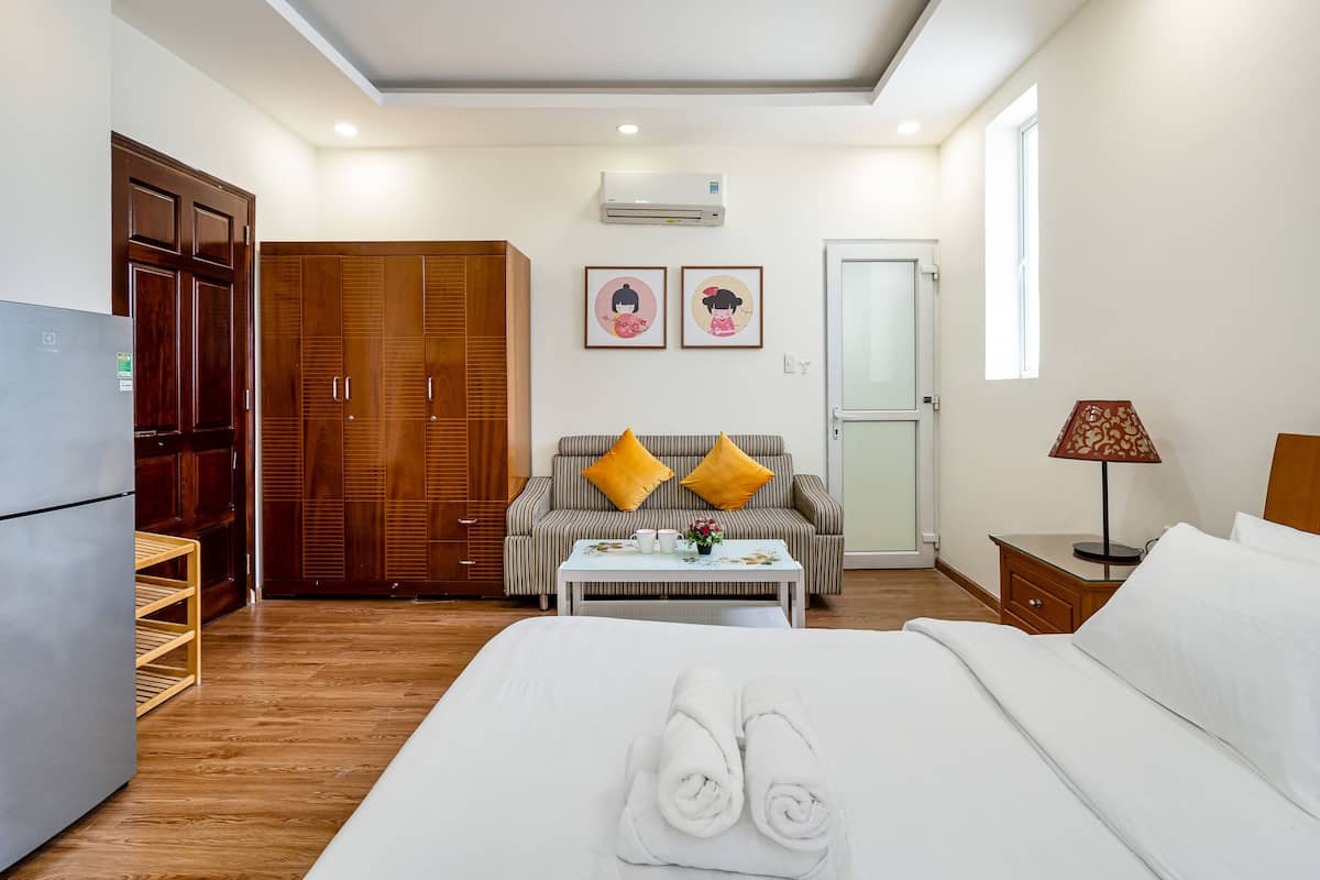 Une chambre d’hôtel comprenant un lit, un canapé, une table avec des serviettes, une armoire, un réfrigérateur et une fenêtre.