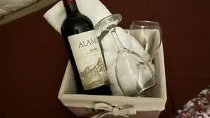 En flaska Alamo-vin, ett glas och en tygservett i en låda som står på sängen.